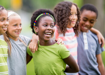 Diverse group of children with arms around eachother smiling and laughing